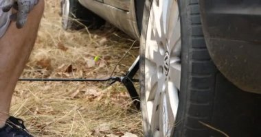 Podolsk, Ukraine: October 25, 2020 Traveler Man is lifting the car to change the rear tire. Tire is damaged. Replacing broken vehicle tire on the grass