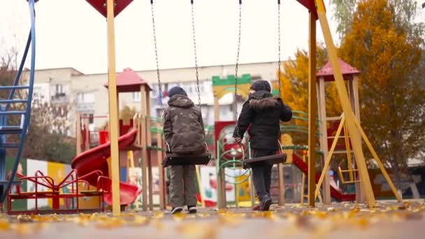 Barn åker en sväng på lekplatsen. Pojkar 8 10 år gamla i varma kläder går i stadsparken — Stockvideo