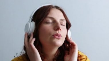 Happy carefree millennial woman listening to music in headphones singing, enjoying audio in earphones at home indoors