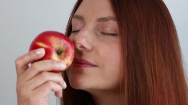 Happy young woman holding fresh ripe red apple in hand and smells organic fruit isolated on gray background.