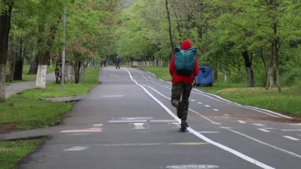 Joven viajero en ropa deportiva con una mochila monta un scooter en un parque de la ciudad — Vídeos de Stock