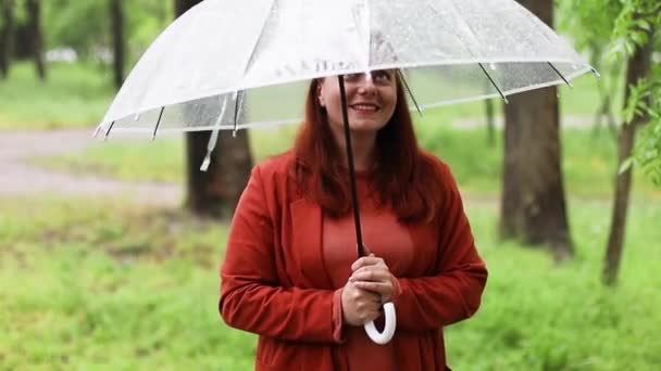 Beautiful happy woman holding transparent umbrella standing outside in raining day. Raindrops. — Stockvideo