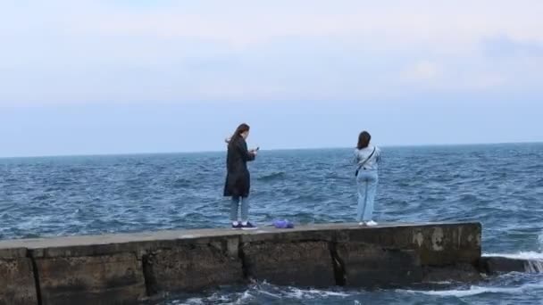Odessa, Ukraine, May, 29 th, 2021: Young girls teenagers are photographed on a stone pier against the background of the sea waves. Blue waves crashing against rocks. — Stock Video