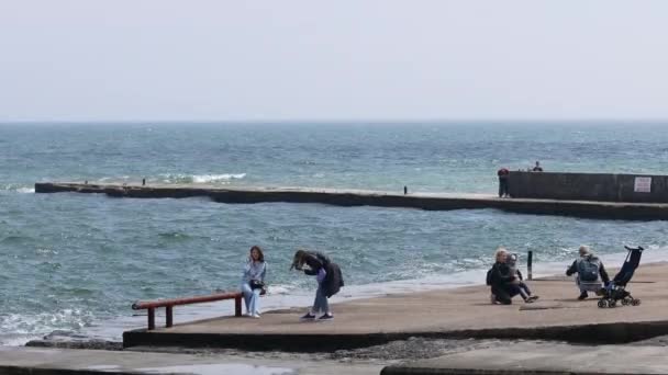 Personas y familias caminan a lo largo de la orilla del mar en un día soleado de primavera. Tormenta fuerte. Olas golpeando la orilla — Vídeos de Stock