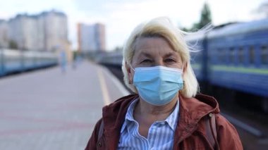Koronavirüs Covid-19 salgını sırasında halk tren istasyonunda yüzünde koruyucu maske takan yetişkin sarışın kadın. Trenle seyahat et.