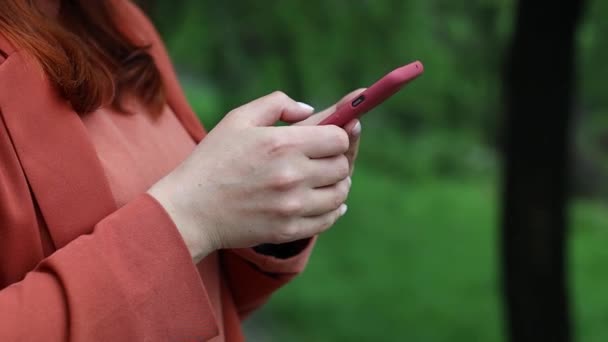 モバイルアプリ技術を使ってスマートフォンを持っている白人女性屋外。市内公園でオンラインソーシャルネットワークアプリケーションをチェックしている若い人. — ストック動画