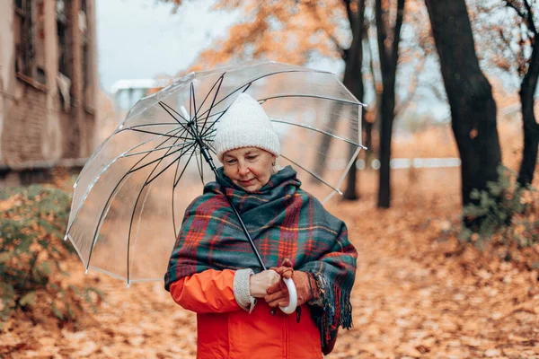 Portrait d'une femme adulte coiffée d'un chapeau blanc et d'un foulard à carreaux chaud sous un parapluie transparent dans un parc d'automne à l'extérieur. Tapis doré tombant feuilles d'automne — Photo
