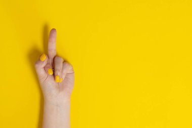 Female hands showing middle fingers gesturing, fuck on a yellow background.