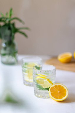 Ev yapımı ferahlatıcı limonata, limon dilimleri ve arka planda vazoda çiçek buketi olan buzlu bardaklar.