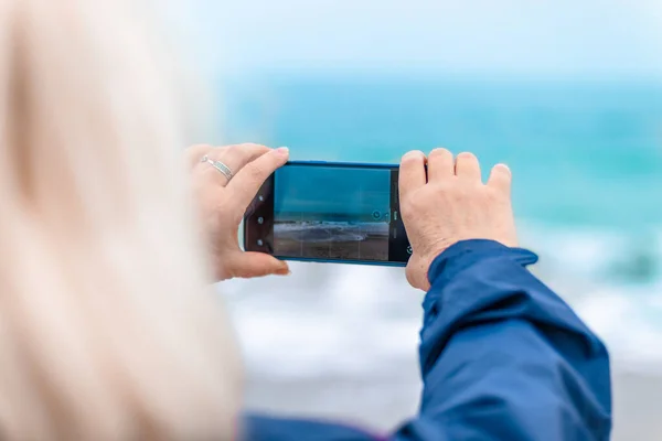 白人ブロンドの女性は海の近くのビーチでスマートフォンで写真やビデオを記録します 休暇のコンセプト — ストック写真