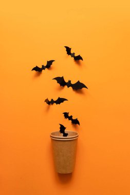 Siyah yarasaların Cadılar Bayramı tatili kavramı turuncu arka planda kağıt bardaktan uçar. Korku ve tehlike tatili