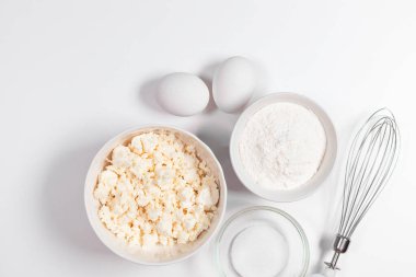 Süzme peynirli krep hazırlamak için gerekli malzemeler. Kahvaltı için beyaz bir masada süzme peynir, yumurta ve un. Üst manzara, düz uzanma