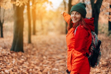 Sırt çantalı çekici beyaz kadın seyahat yönünü, arkadan manzarayı, ormanda yürüyüşü, sonbahar manzarasını gösteriyor.