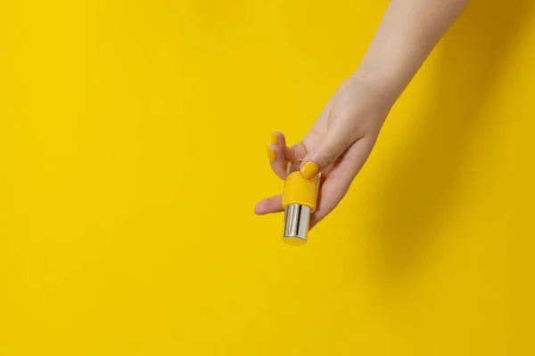 Bright yellow manicure with a bottle of nail polish in hands on yellow background. Flat lay style. Nail design copy space