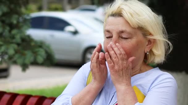 Allergie voor stof. Coronavirus Covid 19 Volwassen blonde vrouw niest terwijl ze buiten in het park zit. Allergie voor planten en bloemen stuifmeel. — Stockvideo