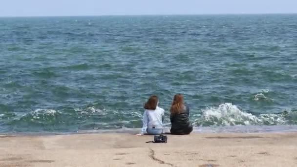 İki kız arkadaş taş bir iskelede oturuyor ve güzel deniz manzarasının tadını çıkarıyorlar. — Stok video