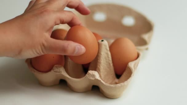 Коричневі органічні курячі яйця в коричневому паперовому лотку розміщені на білому столі. Концепція здорового харчування та органічного білкового сніданку — стокове відео