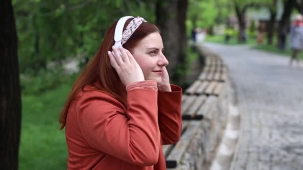 Fehér boldog nő fehér fejhallgatót visel zenét hallgat az utcán szabadban. — Stock videók