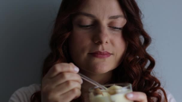 Gros plan portrait de fille caucasienne aux cheveux bouclés mangeant un délicieux dessert crémeux, appréciant le goût sur fond gris — Video