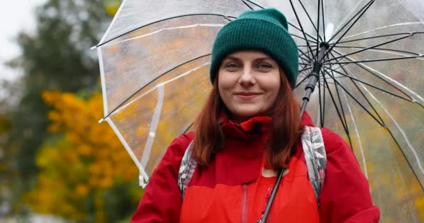 Gülümseyen güzel kadın yağmurlu havanın tadını çıkarıyor. O, şemsiyenin altında duruyor. Sonbahar havası — Stok video