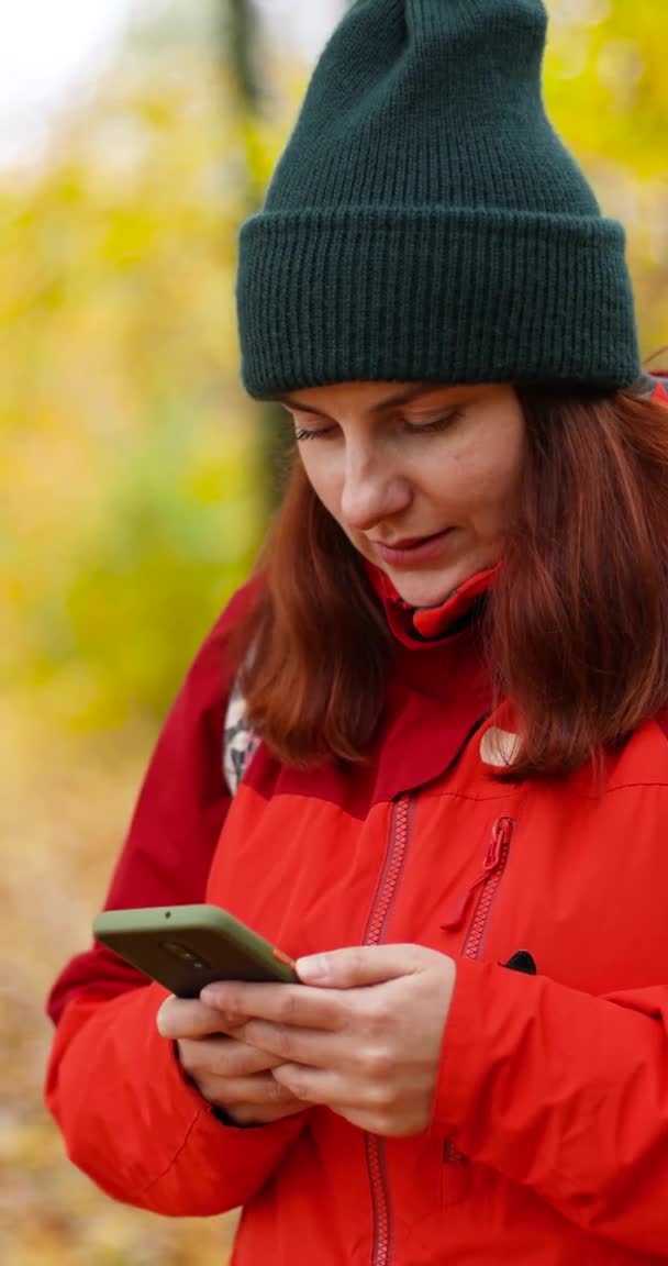 Joven viajero turístico chica con una mochila está escribiendo un mensaje en el teléfono en un hermoso sendero del bosque de otoño — Vídeo de stock