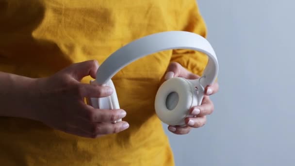 Manos femeninas sosteniendo auriculares inalámbricos blancos sobre fondo gris — Vídeos de Stock