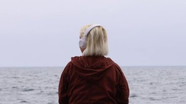 Sarışın bir kadının müzik dinleyip denize baktığı arka plan.
