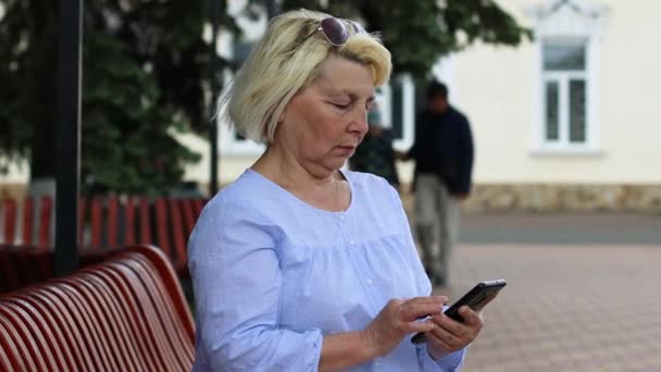 Aantrekkelijke, succesvolle en gelukkige vrouw van middelbare leeftijd die mobiele telefoon gebruikt voor sms 'en of sociale media terwijl ze buiten in het stadspark zit. — Stockvideo