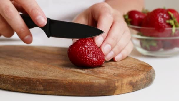 La mano femminile taglia una fragola su una tavola di legno in cucina. — Video Stock