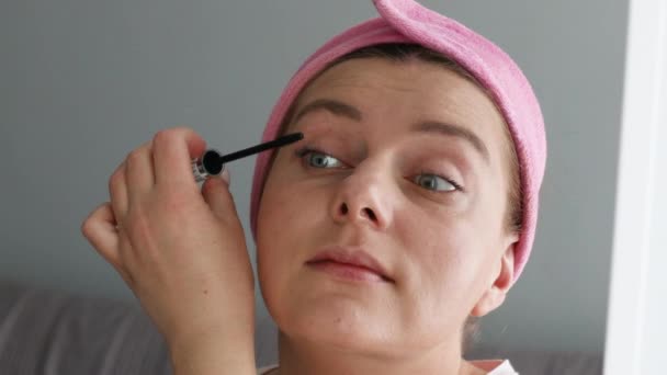 Piękna kobieta model robi makijaż za pomocą czarnej szczotki do rzęs patrząc w lustrze w domu — Wideo stockowe