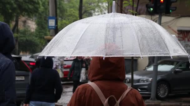 Mujer con paraguas transparente bajo la lluvia en una ruidosa calle de la ciudad. Mal tiempo frío — Vídeos de Stock