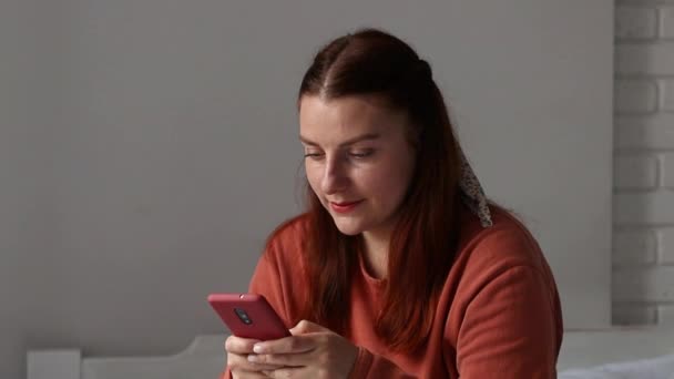 Jeune fille millénaire caucasienne utilisant un smartphone. Jeune fille tenant un téléphone portable, bavardant sur les réseaux sociaux, assise sur le canapé dans le salon. Communication en ligne — Video