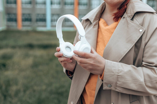 Female hand holding stylish white wireless headphones on green blurred background with copy space