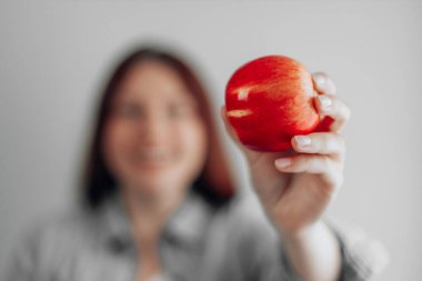 Gri arka planda kırmızı bir elma tutan genç bir kadın. Sağlıklı beslenme. Elma vitamini..