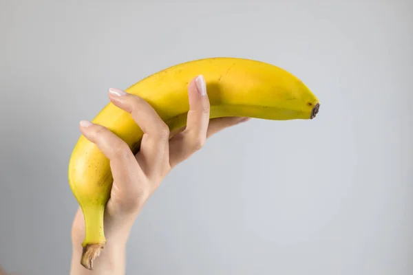 Mão Feminina Segurando Uma Banana Amarela Fundo Cinza Colorido Brilhante — Fotografia de Stock
