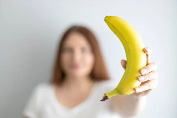 Jovem segurando banana amarela madura em fundo cinza. Conceito de nutrição de frutas — Fotografia de Stock