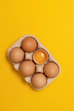 Kahverengi tavuk yumurtaları ve sarı arka planda yumurta sarısı olan kırık bir yumurta. Doğal sağlıklı yiyecekler