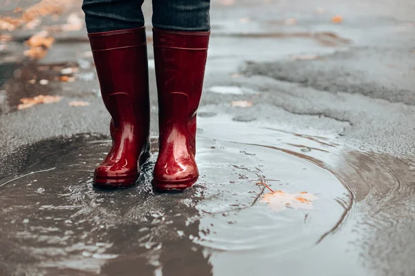 Mulher com botas de borracha vermelha escura pulando na poça, close-up. Tempo chuvoso — Fotografia de Stock