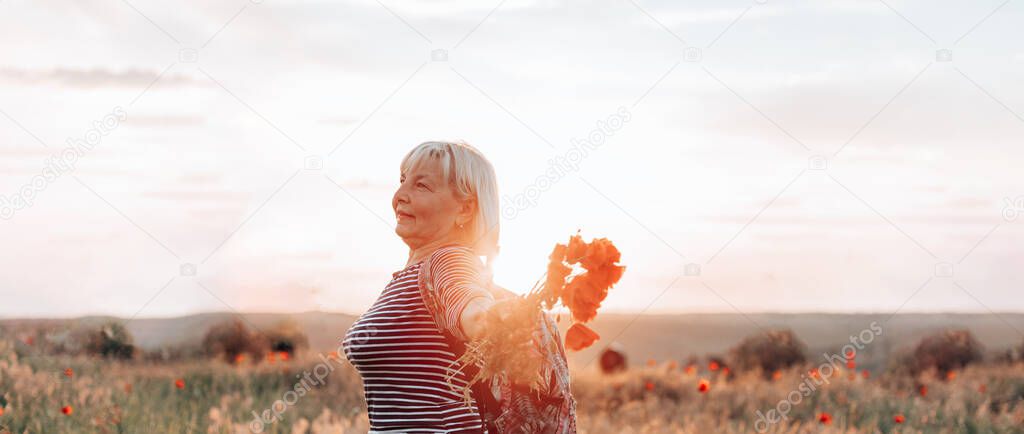 Adult woman tourist with backpack and poppy flower bouquet at sunset in the field. Summer vacation. Happy girl with blond hair enjoying the sun.