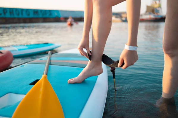 Close up shot of a young surfer girl strapping on her leash by the sea or ocean. — Stock Photo, Image