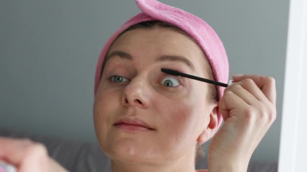 Vacker kvinna modell gör makeup med svart ögonfransborste medan du tittar i spegeln hemma. Modern kvinna applicerar mascara på sina ögonfransar. — Stockvideo