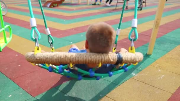 Vue arrière d'un enfant garçon heureux se balançant sur une balançoire et profitant d'une belle journée d'été. — Video