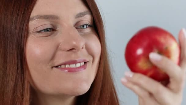 손에 신선하게 익은 붉은 사과 열매를 들고 있는, 곱슬곱슬 한 젊은 여자가 회색 배경에서 분리되어 있다. 긴장을 푸는 휴가 개념. — 비디오