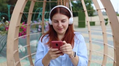 Bin yıllık gülümseyen bir kadının portresi. Akıllı telefon kullanıyor ve kulaklıkla sokak ortasında müzik dinliyor.
