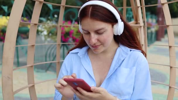 Caucasienne belle jeune femme prenant des écouteurs et écoutant de la musique à l'extérieur au parc de la ville au coucher du soleil — Video