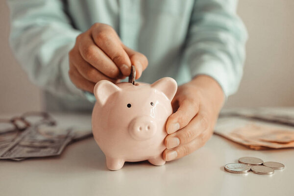 Female putting money coin in piggy bank at home. Business finance saving and investment concept.