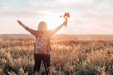 Sırt çantalı bir kadın turist buğday tarlasını geçerek yol boyunca yürüyor. Turizm, seyahat ve sağlıklı yaşam tarzı konsepti.