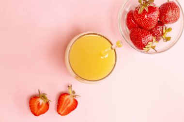 Tabakta taze çilek ve pembe masada bir bardak portakal suyu.