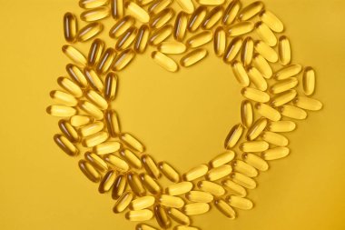 Balık yağı omega 3 jel kapsülleri sarı arka planda kalp şeklinde, yakın plan, düz yatış. Sağlıklı Beslenme.