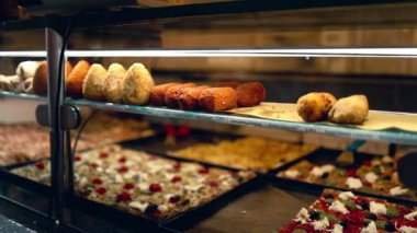 Lezzetli İtalyan sokak yemekleri, arancini ve Roma 'da sıcak bir fırında sergilenen taze pişmiş pizza dilimleri. Ilık ışıklandırma, otantik Akdeniz 'in dokularını ve renklerini vurguluyor